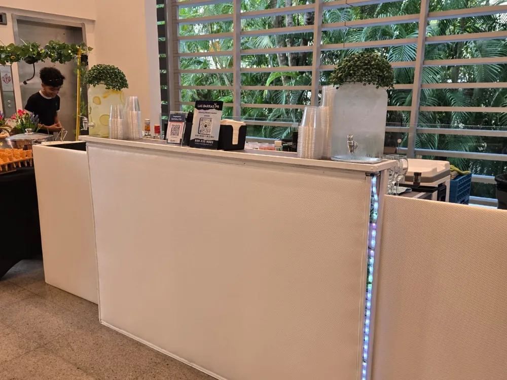 Barra blanca montada con botellas y cristalería, lista antes del evento
